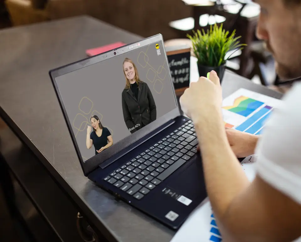 Um homem está em frente ao computador assistindo uma aula do curso de acessibilidade da Fundação Dorina. O computador está em uma bancada escura.